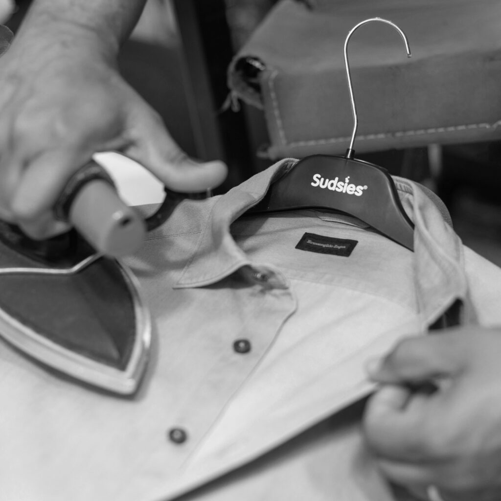 Garment being professionally pressed on a Sudsies hanger by Sudsies dry cleaning specialists